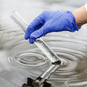 Researcher holds a test tube with water in a hand in blue glove